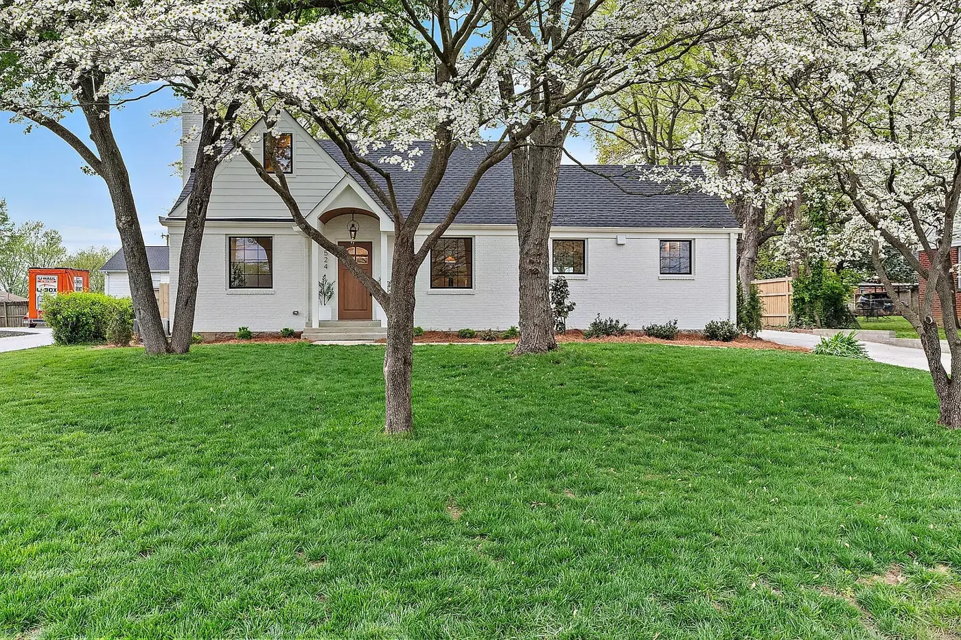 White painted-brick cottage beneath mature dogwood trees